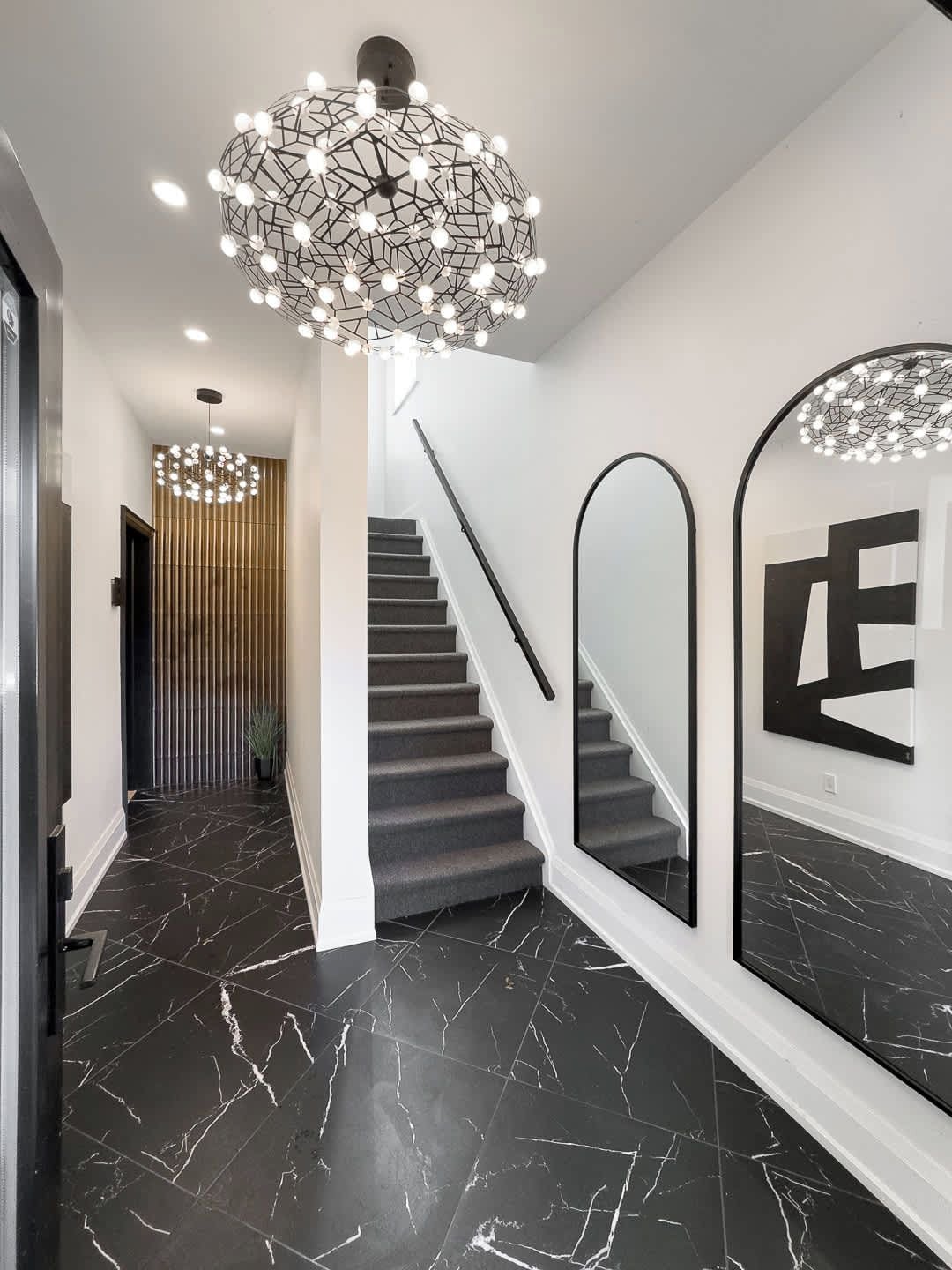 A modern interior with a staircase, black marble flooring, and contemporary lighting fixtures.
