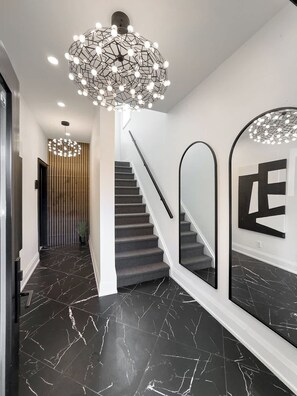 Un intérieur moderne avec un escalier, un revêtement de sol en marbre noir et des luminaires contemporains.