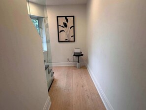 Un couloir doté d’un plancher en bois, d’une œuvre d’art encadrée au mur et d’une petite table sur laquelle se trouve un panier.