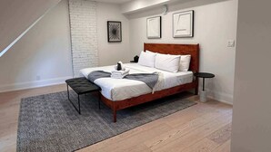 A bedroom with a bed, a bench, a small table, and a patterned rug. - Cozy West End Gem! Bright 2BR w Huge Private Deck (Toronto)