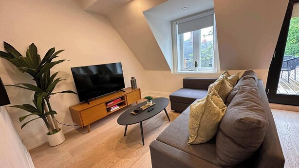 A modern living room with a flat-screen TV, a sofa, a coffee table, and a potted plant. - Cozy West End Gem! Bright 2BR w Huge Private Deck (Toronto)