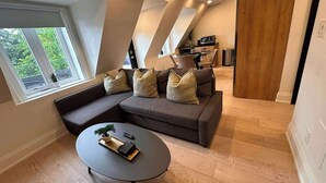 A modern living room with a sectional sofa, a round coffee table, and a view of the outdoors through large windows. - Cozy West End Gem! Bright 2BR w Huge Private Deck (Toronto)