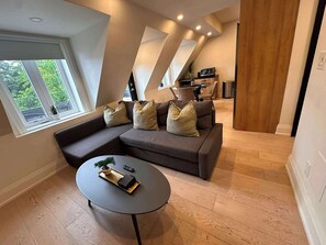 Un salon moderne avec un canapé d’angle, une table basse ronde et une vue sur l’extérieur grâce à de grandes fenêtres.
