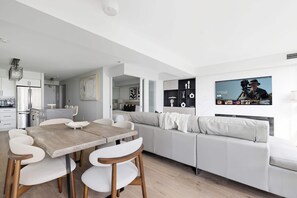 A modern living space with a dining area, sofa, and a TV displaying a video game. - Upscale 2BR Condo Downtown TO Gem w Parking | Parking Available (Toronto)