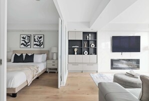 A modern bedroom with a bed, bedside tables, a nightstand, a built-in wardrobe, a TV, and a seating area with a sofa and a coffee table. - Upscale 2BR Condo Downtown TO Gem w Parking | Parking Available (Toronto)