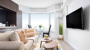 A modern living room with a sofa, a coffee table, a flat-screen TV mounted on the wall, and a large window providing a view.
