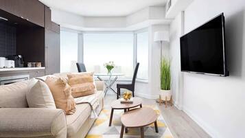 A modern living room with a sofa, a coffee table, a flat-screen TV mounted on the wall, and a large window providing a view.