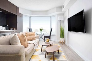 A modern living room with a sofa, a coffee table, a flat-screen TV mounted on the wall, and a large window providing a view.