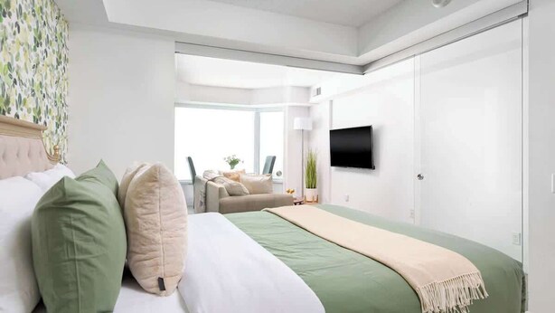 A modern bedroom with a bed, a sofa, a TV, and a large window.