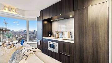 A modern kitchen with dark wood cabinets, a built-in oven, and a large window offering a city view.
