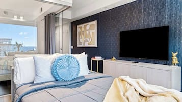 A modern bedroom with a large bed, a flat-screen TV, and a city view.