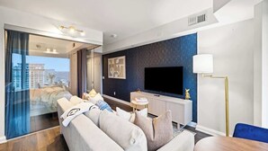 Une chambre d’hôtel moderne dotée d’un grand téléviseur à écran plat, d’un canapé, d’une table à manger et offrant une vue à travers une porte vitrée.