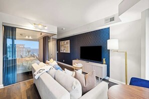 Quarto de hotel moderno com uma televisão de tela plana grande, um sofá, uma mesa de jantar e vista através de uma porta de vidro.