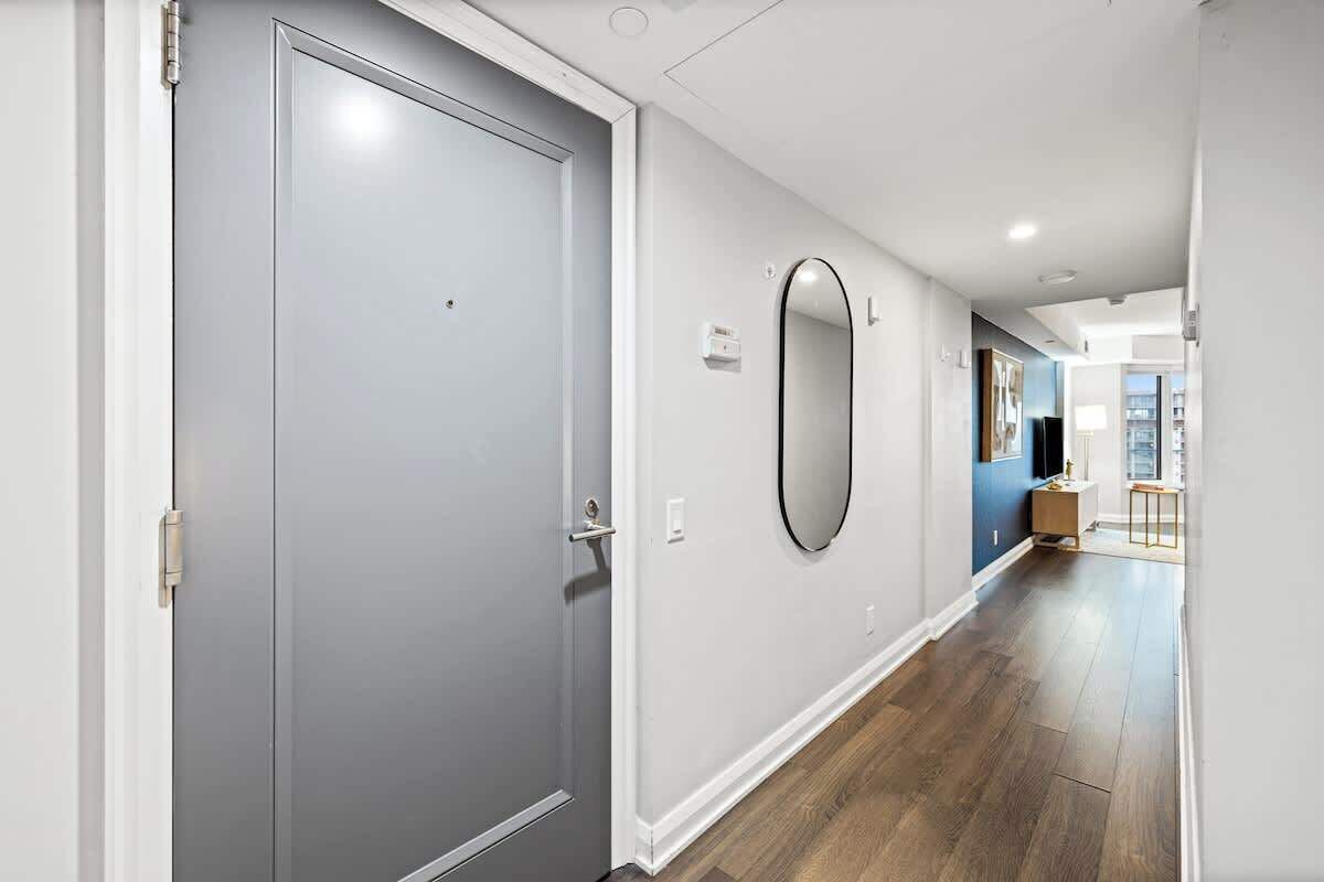 A hallway with a grey door, a wall-mounted mirror, and a wooden floor.