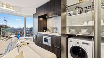 A modern kitchen with a built-in washer and dryer, a large window with a city view, and a cozy seating area with a sofa.