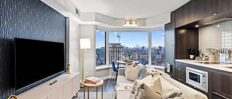 A modern living room with a large flat-screen TV, a sofa, a dining area, and a kitchen with a microwave.