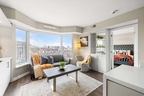Eine moderne Wohnung mit großem Fenster, einer Couch, einem Esstisch und einem Bett mit Blick auf die Stadt.
