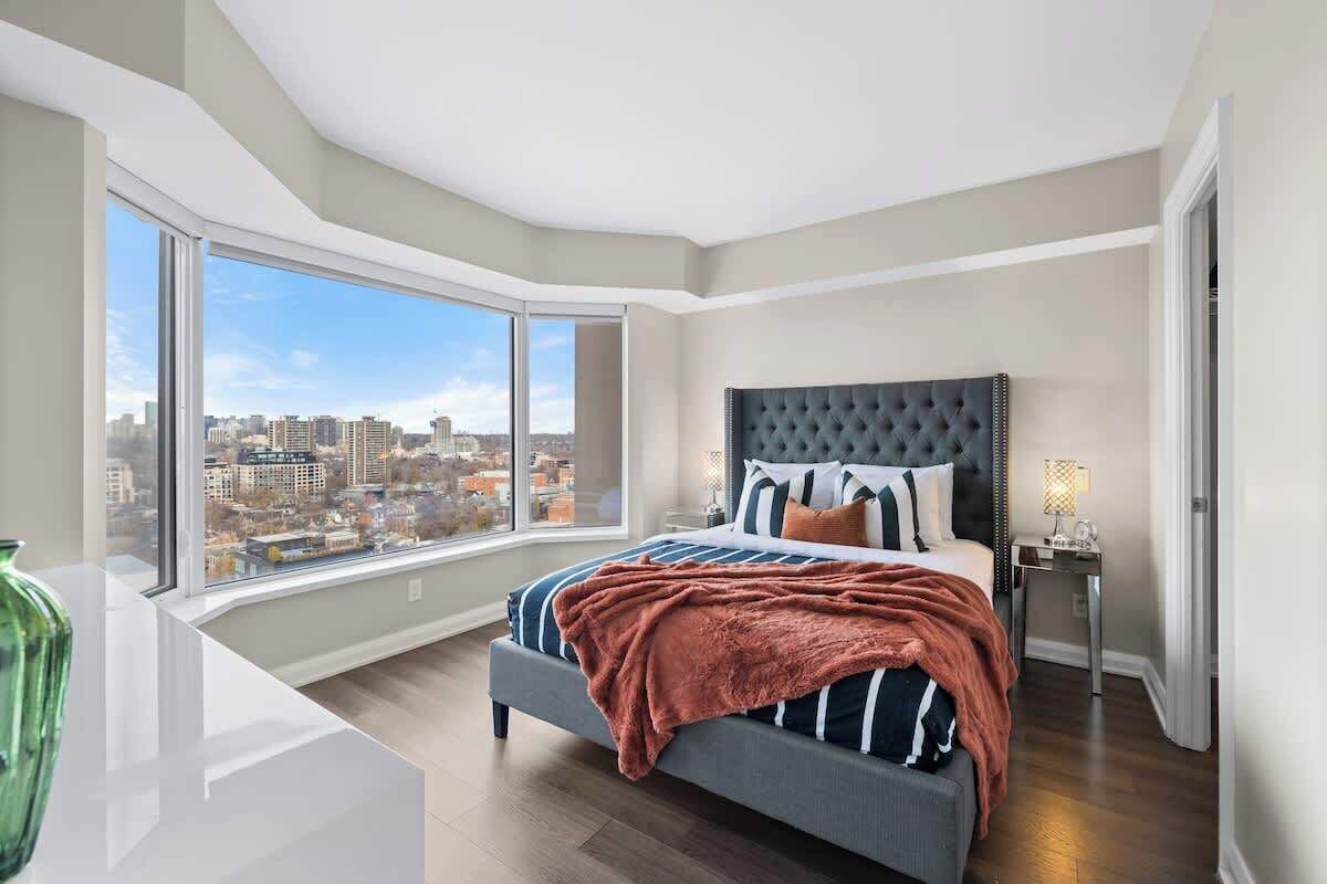 A bedroom with a large window, a bed with striped bedding, and a city view.