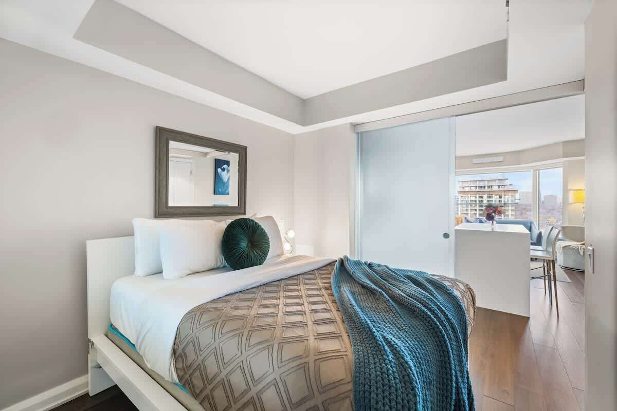 A modern hotel room with a bed, a desk, and a view of the city.