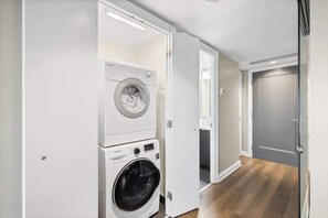A laundry room with stacked washers and dryers, a wooden floor, and a door leading to another room.