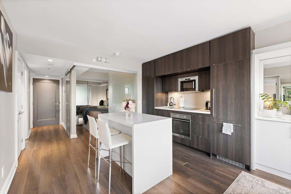 A modern kitchen with a central island, dark cabinetry, and stainless steel appliances.