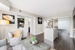 A modern living room with a sofa, a coffee table with a plant, and a kitchen area with a refrigerator and cabinets.