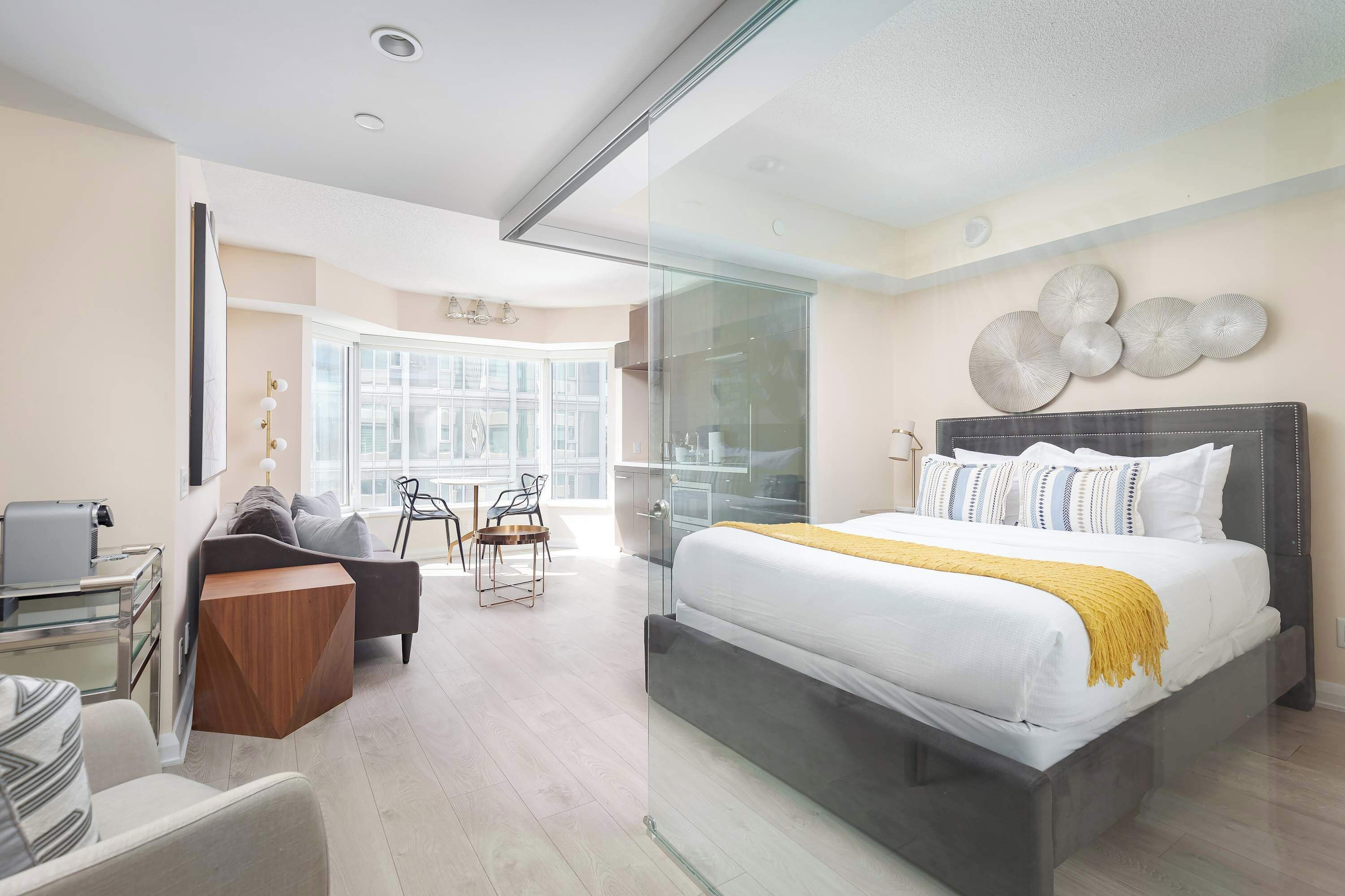 A modern hotel room with a large bed, a desk, a chair, and a glass partition.
