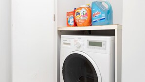 A compact, white washing machine with a digital display, placed in a small laundry room with a wooden floor. - Designer 4 Seasons Luxury Bldg of Yorkville! (Toronto)