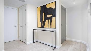 A hallway with a minimalist design, featuring a white door, a white wall, and a large abstract painting.