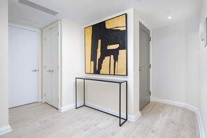 A hallway with a minimalist design, featuring a white door, a white wall, and a large abstract painting.