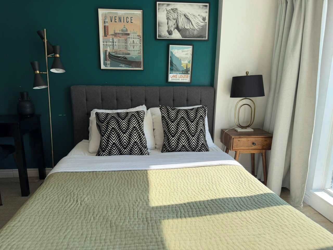 A bedroom with a bed, two patterned pillows, a bedside table with a lamp, and wall art.