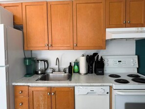 A kitchen with wooden cabinets, a white stove, a dishwasher, and a coffee maker. - Modern Studio by Massey Hall | Heart of Toronto | Parking Available (Toronto)