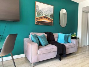 A living room with a teal wall, a sofa with cushions, a mounted TV, and a mirror. - Modern Studio by Massey Hall | Heart of Toronto | Parking Available (Toronto)