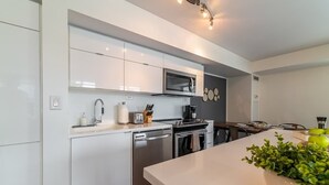 Et moderne køkken med hvide skabe, rustfrie stålgadgetter og en central ø med en grøn plante.