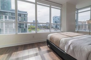 A bedroom with a large window, a bed, and a view of buildings. - Spacious 3BR Downtown Condo with Free Parking | Parking Available (Toronto)