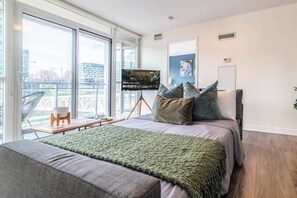 A modern bedroom with a large bed, a television, and a view of the city through large windows. - Spacious 3BR Downtown Condo with Free Parking | Parking Available (Toronto)