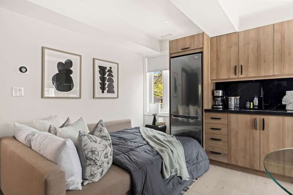 A modern bedroom with a bed, a sofa, and a kitchenette.