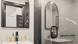 Un baño moderno con tocador blanco, cabina de ducha de vidrio y paredes de mármol.