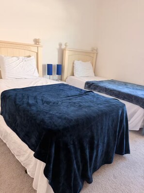 Ein Schlafzimmer mit zwei Betten, eines mit dunkelblauer Bettdecke und das andere mit weißer Bettwäsche.