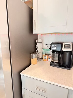 Eine Küche mit Kaffeemaschine, einer Schachtel Karamellcreme und einer Zuckerdose auf der Arbeitsfläche.