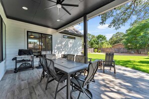 Eine Terrasse im Freien mit Tisch, Stühlen, einem Grill und einem Deckenventilator.