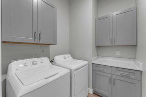 A laundry room with two front-loading washing machines, a dryer, and grey cabinets. - Skier's Cove - Lake Access & Deeded Boat Slip (Granite Shoals)