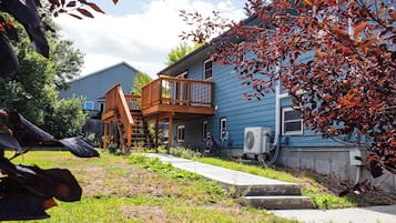 A two-story house with a wooden deck and a small staircase leading to a porch.
