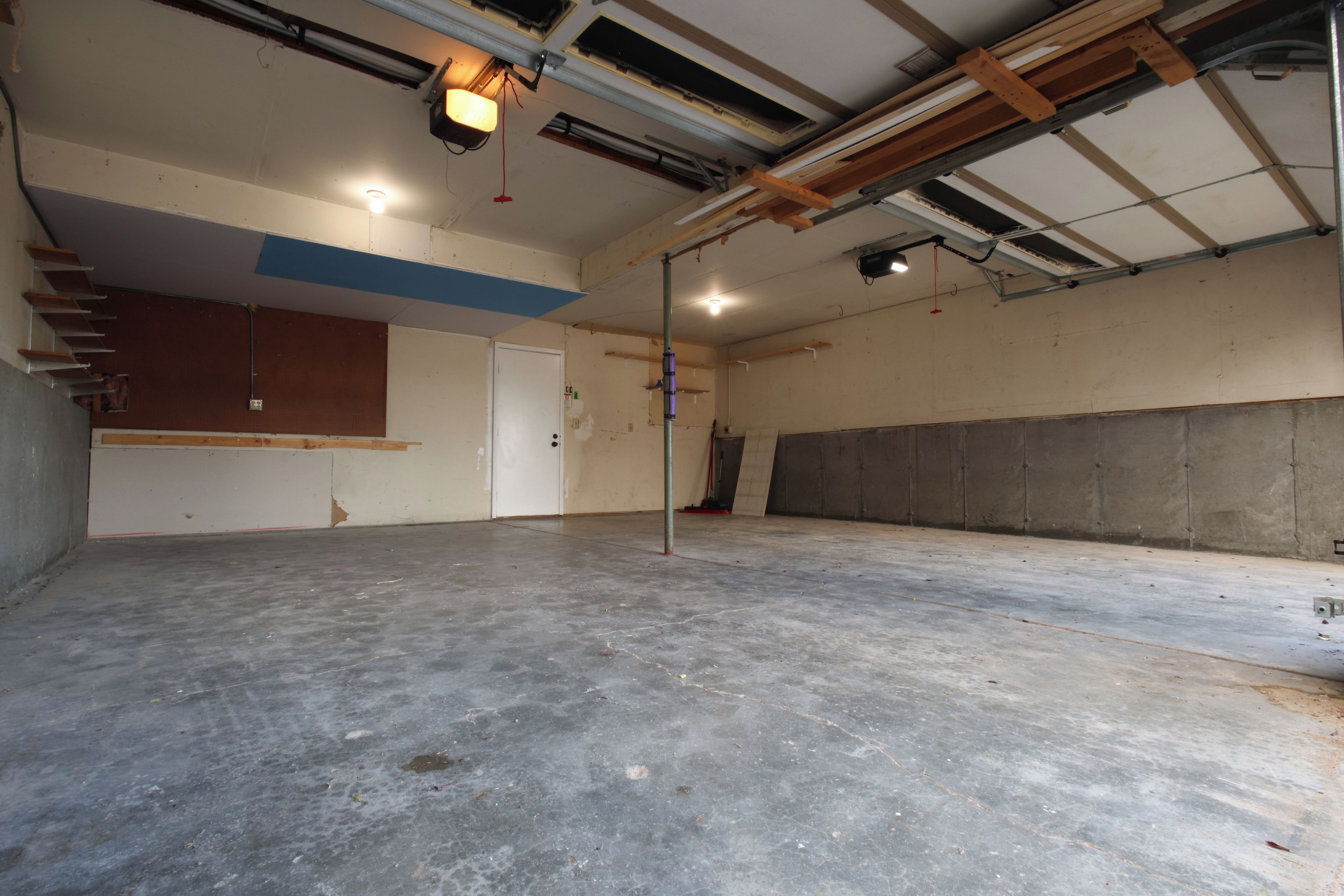 Um espaço amplo e interno com piso de concreto, vigas de teto aparentes e uma porta que dá para outro cômodo.