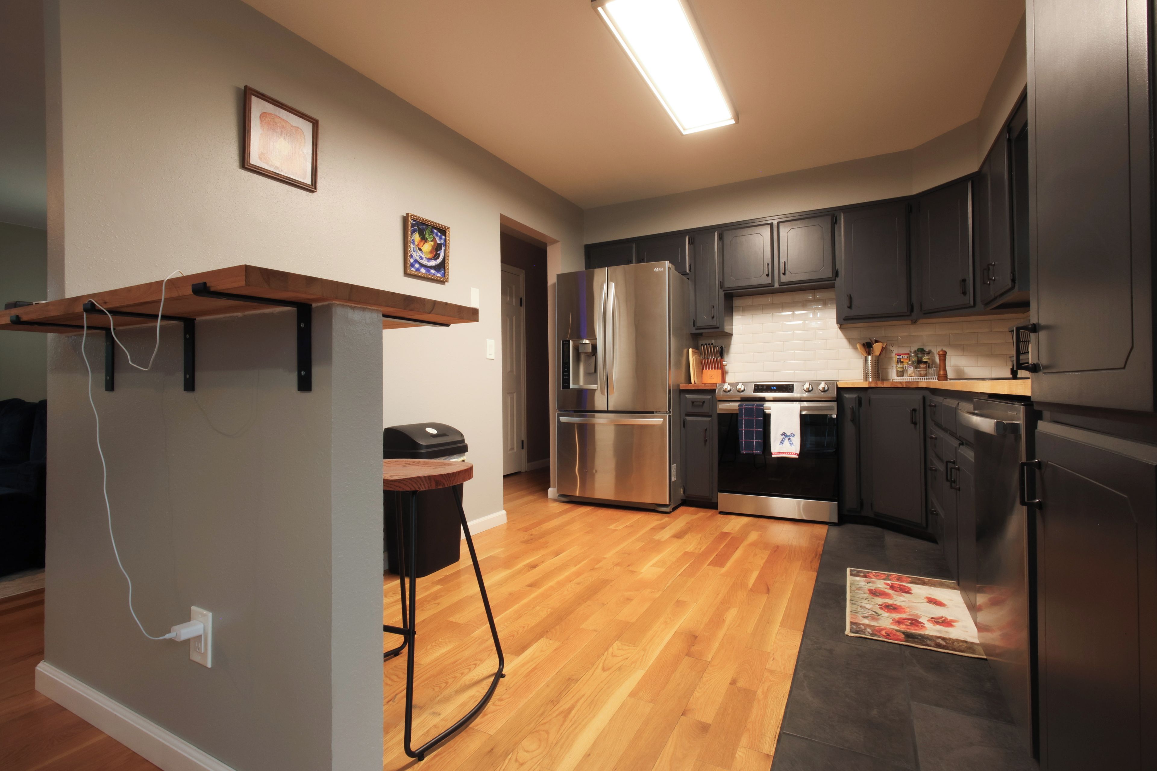 A modern kitchen with stainless steel appliances, wooden flooring, and dark cabinetry.