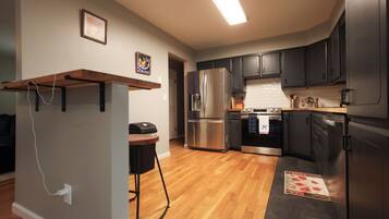 A modern kitchen with stainless steel appliances, wooden flooring, and dark cabinetry.