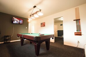 A pool table in a room with a television mounted on the wall, a flag on the wall, and a door leading to another room.