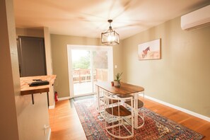 Un espace repas comprenant une table et des chaises, un ventilateur de plafond, un téléviseur fixé au mur et une porte donnant sur un espace extérieur.