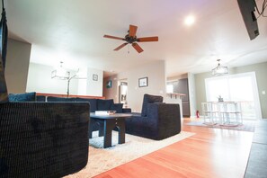 A spacious living room with a ceiling fan, a dining area with a table and chairs, and a kitchen in the background.
