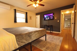 A bedroom with a bed, a ceiling fan, a television, and a hallway.